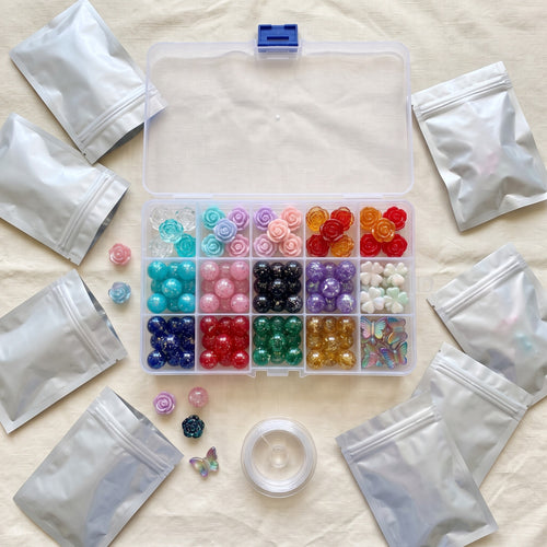 The clear 15-slot bead box full of rose, glow, starry sky, clover and butterfly beads, opened bags around it